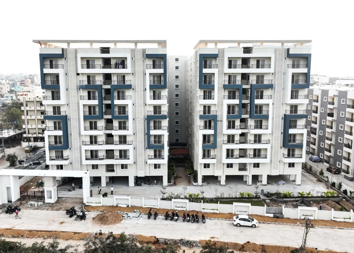Two white apartment towers with slate-grey frames above a boundary wall and an entrance road at HPR Lakefront